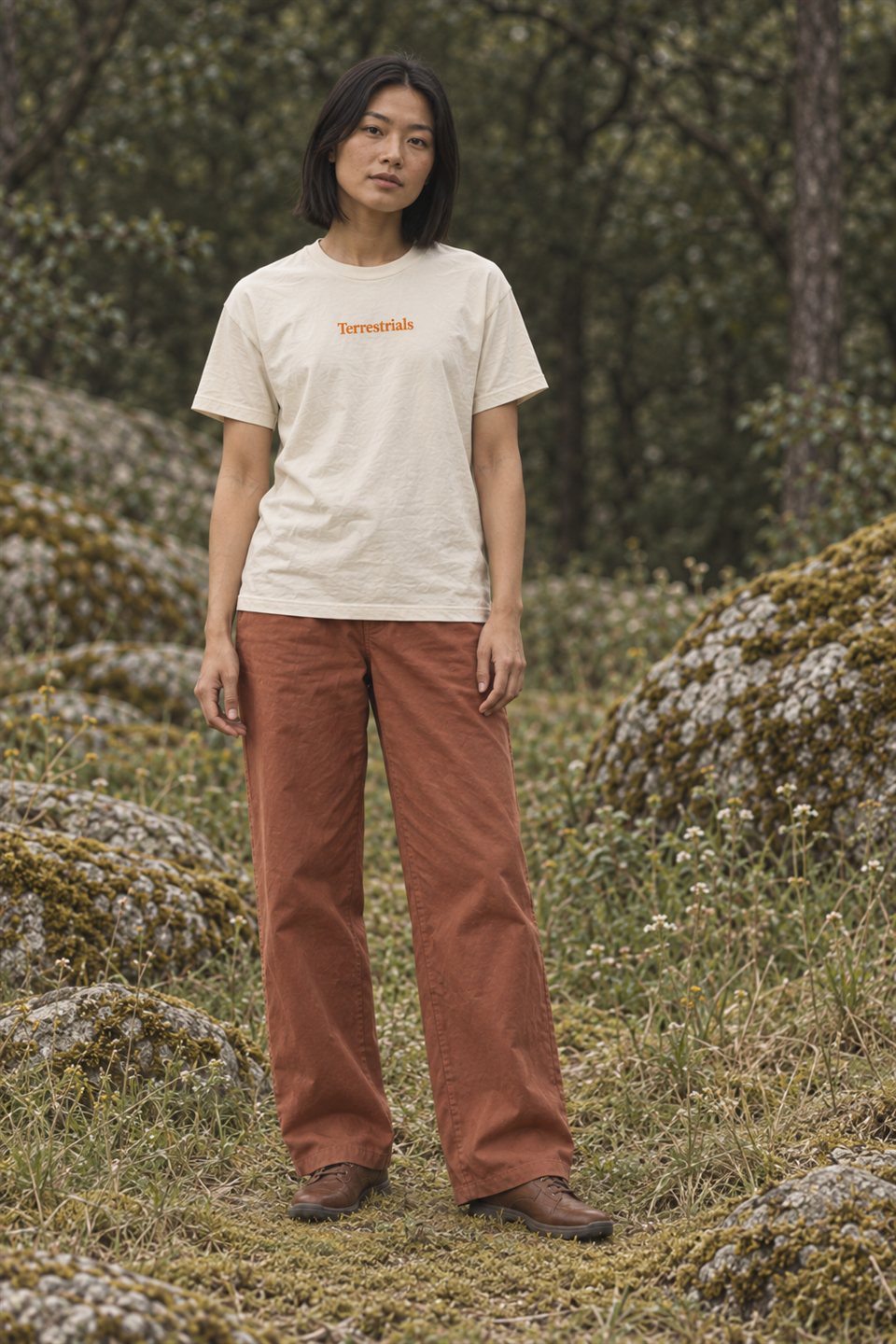 Model wearing a cream Terrestrials shirt among moss-covered rocks